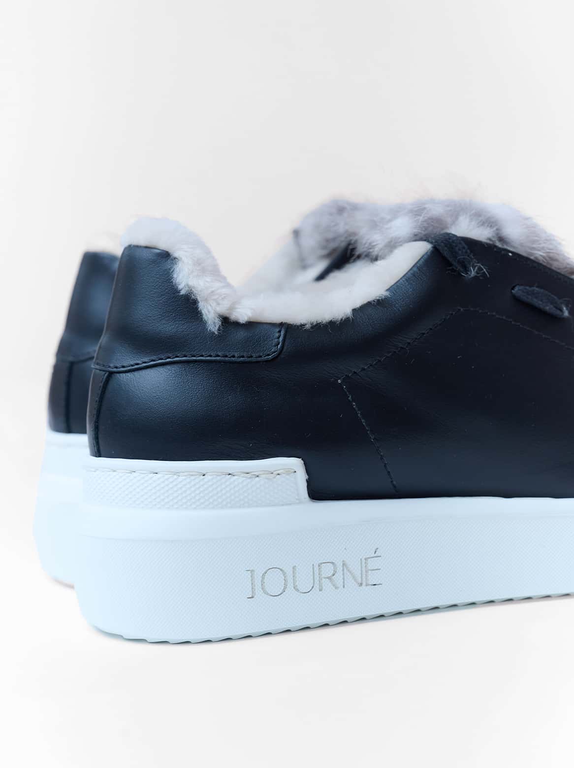 Nahaufnahme der naturgrauen Fellapplikation auf schwarzem Leder und weisser Sohle